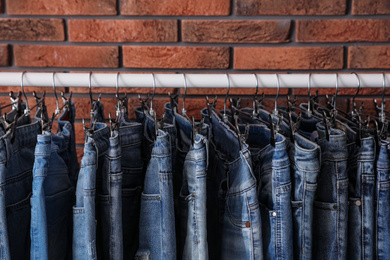 Rack with stylish jeans near brick wall, closeup