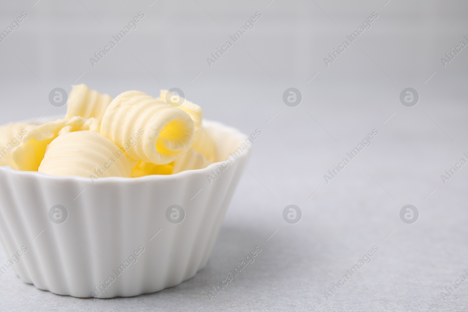 Photo of Tasty butter curls in bowl on light grey table, closeup. Space for text