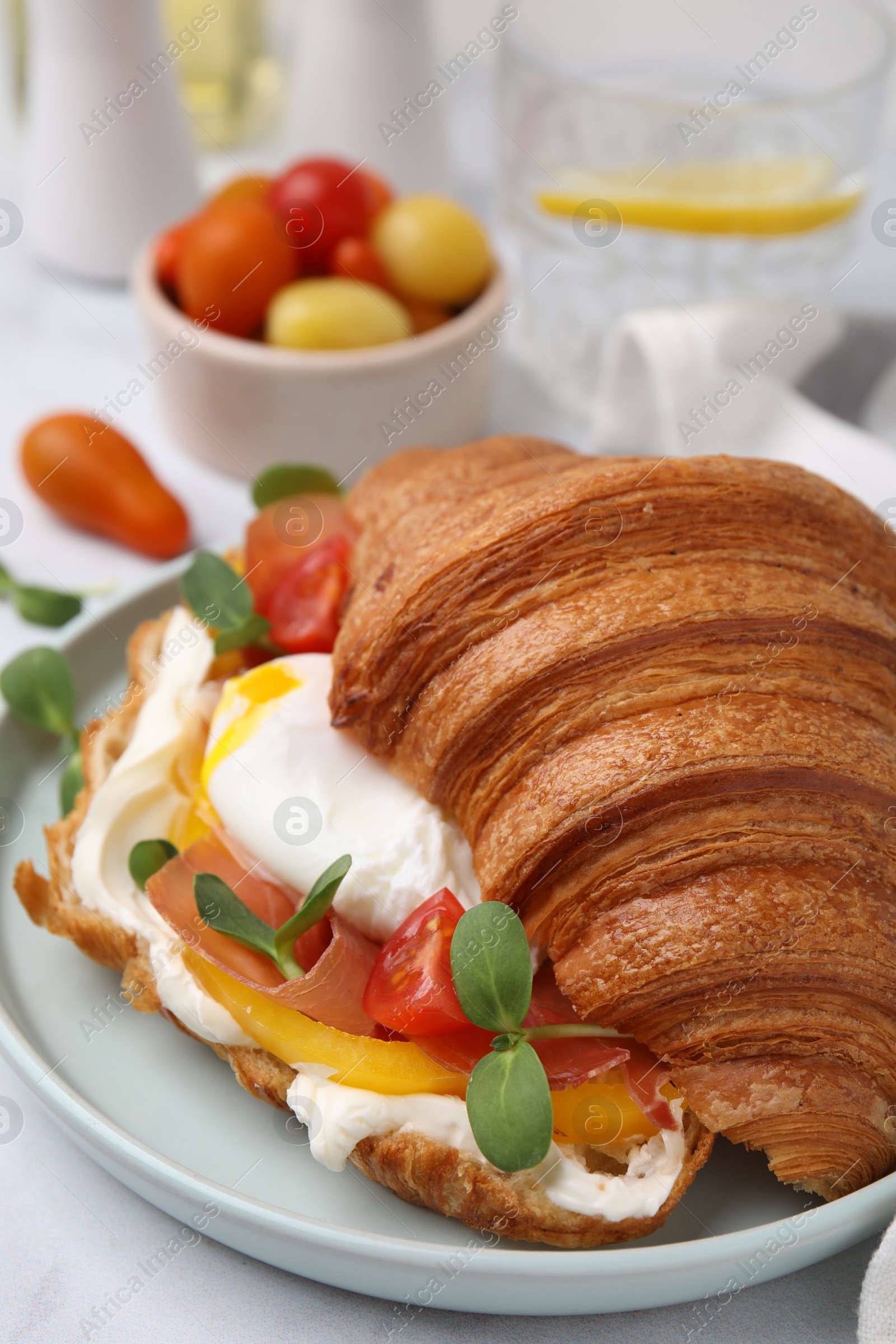 Photo of Tasty croissant with fried egg, tomato and microgreens on white table, closeup