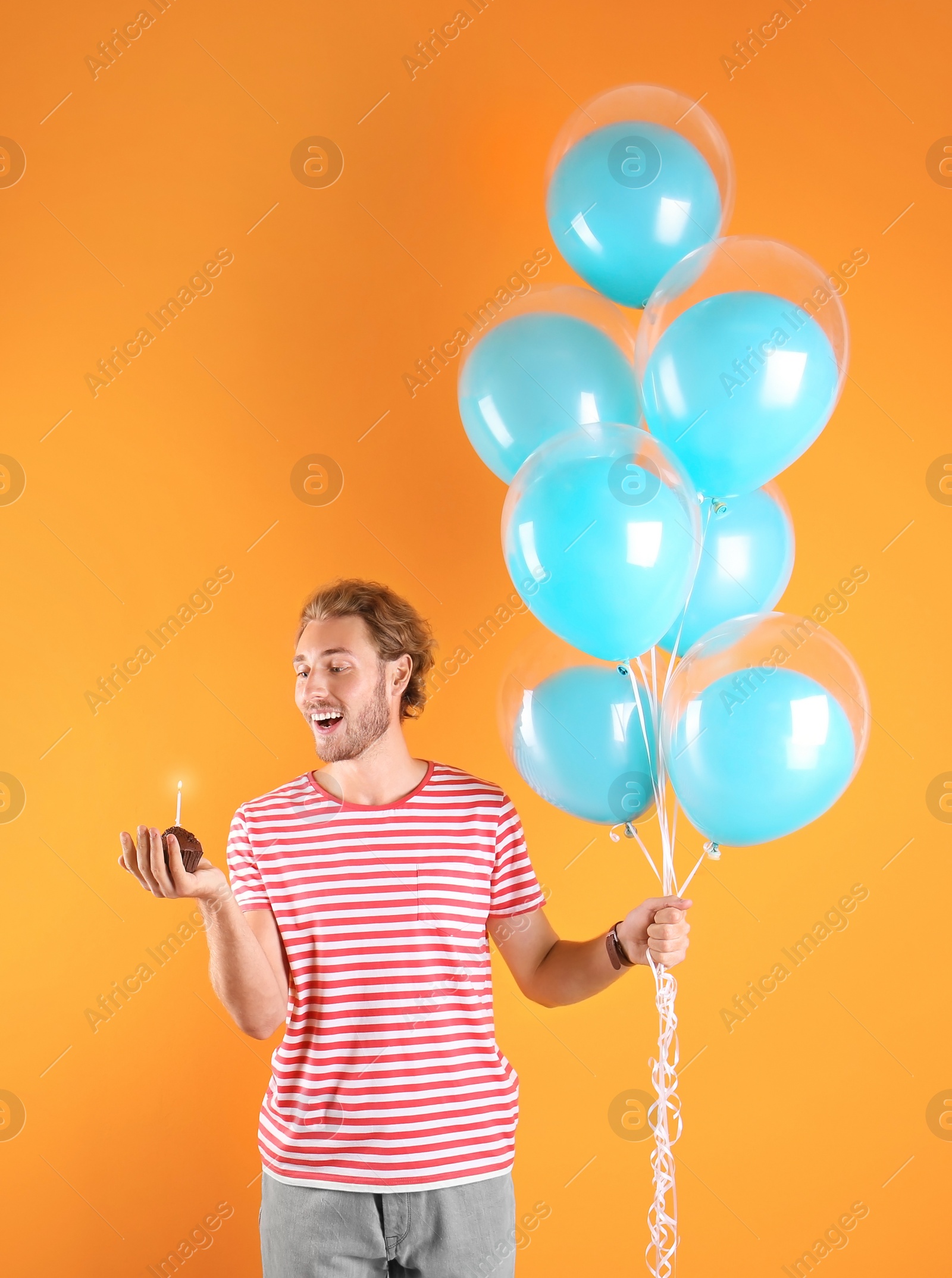 Photo of Young man with birthday muffin and air balloons on color background