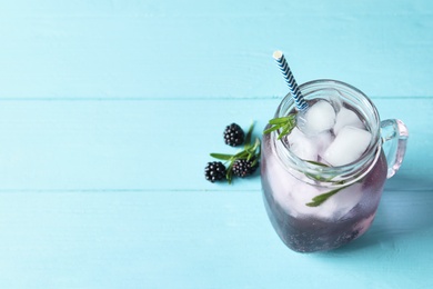 Image of Refreshing blackberry drink with rosemary and ice cubes in mason jar on turquoise wooden table. Space for text