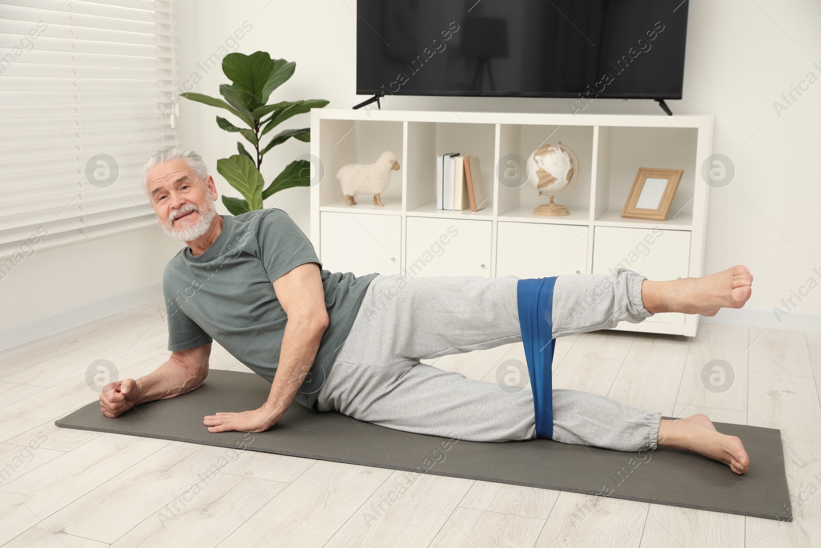 Photo of Senior man doing exercise with fitness elastic band on mat at home