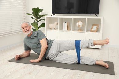 Senior man doing exercise with fitness elastic band on mat at home