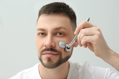 Photo of Man using metal facial roller on light background