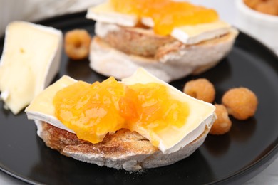 Photo of Tasty sandwiches with brie cheese, fresh raspberry and apricot jam on black plate, closeup