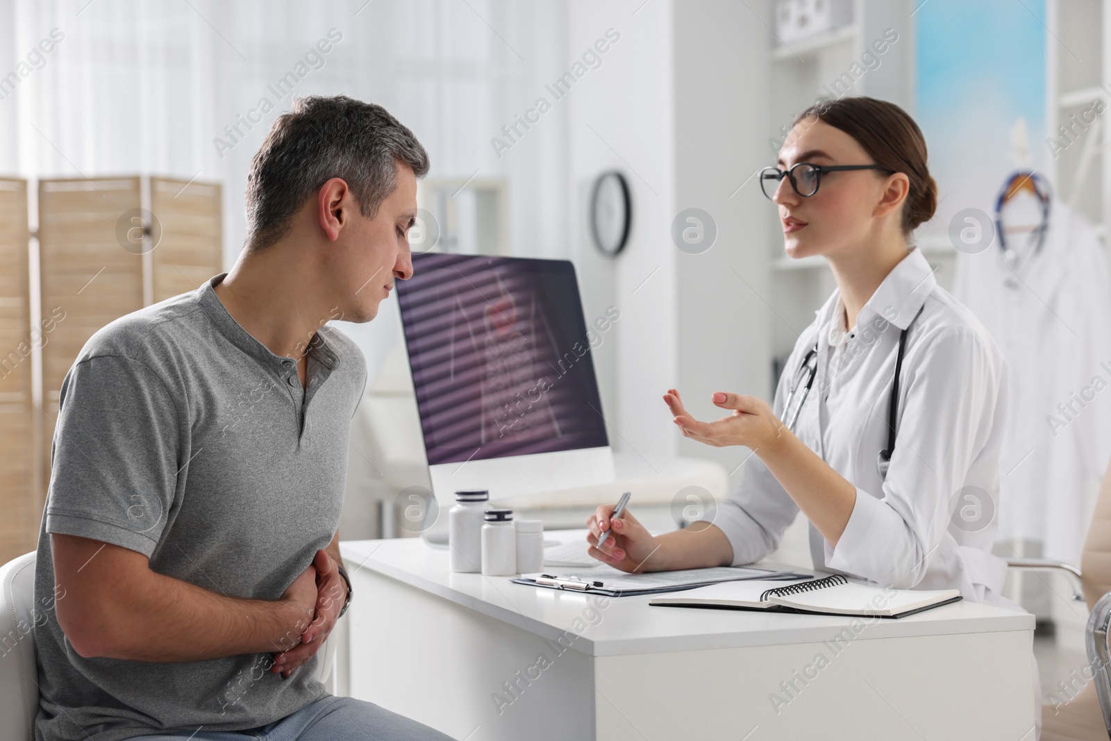 Photo of Gastroenterologist consulting patient with stomach pain at table in clinic