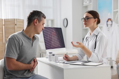 Photo of Gastroenterologist consulting patient with stomach pain at table in clinic