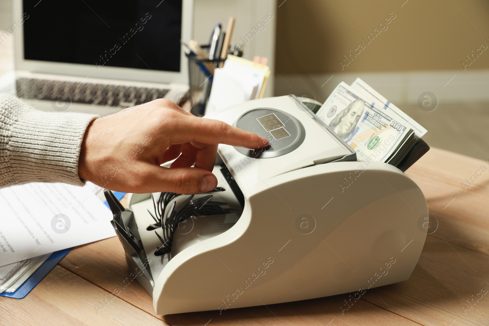 Photo of Man using banknote counter at wooden table indoors, closeup