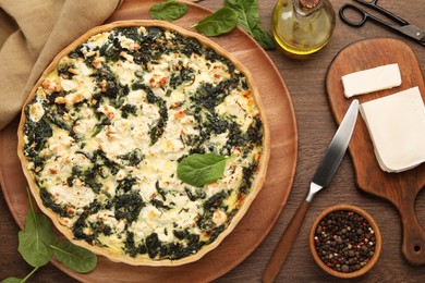 Delicious homemade spinach quiche, spices and knife on wooden table, flat lay