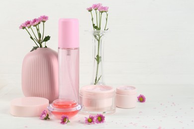 Photo of Homemade cosmetic products and beautiful flowers on white wooden table. Space for text