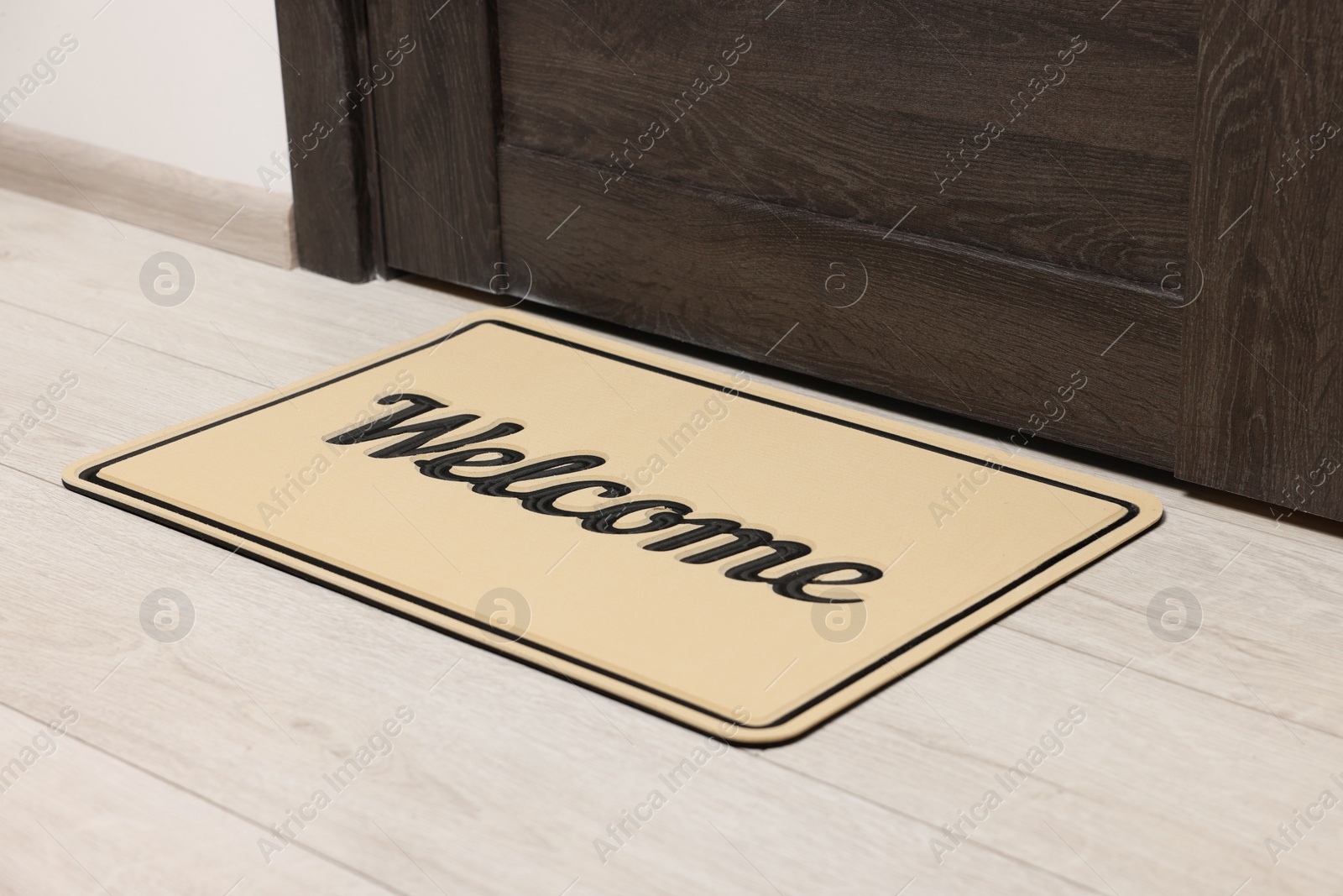 Photo of Beige doormat with word Welcome on white floor near entrance