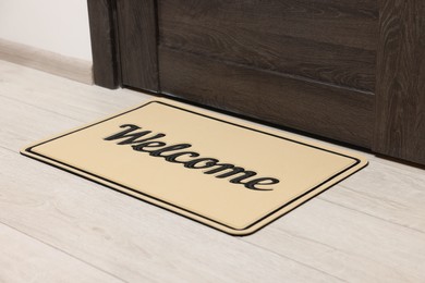 Photo of Beige doormat with word Welcome on white floor near entrance