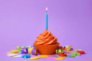 Photo of Delicious birthday cupcake with orange cream and burning candle on violet background