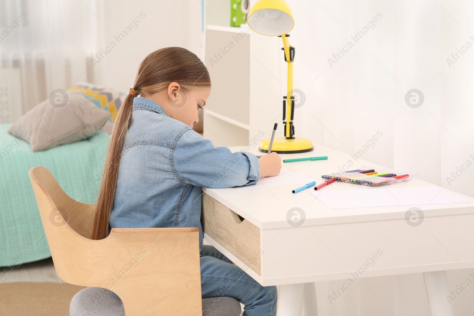 Photo of Cute little girl drawing with markers at desk in room. Home workplace