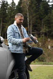 Photo of Man pouring hot drink from metallic thermos into cup lid near car outdoors