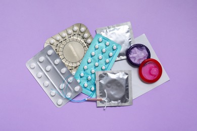 Photo of Contraceptive pills, condoms and intrauterine device on violet background, flat lay. Different birth control methods