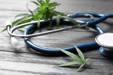 Photo of Hemp leaves and stethoscope on grey wooden table, closeup