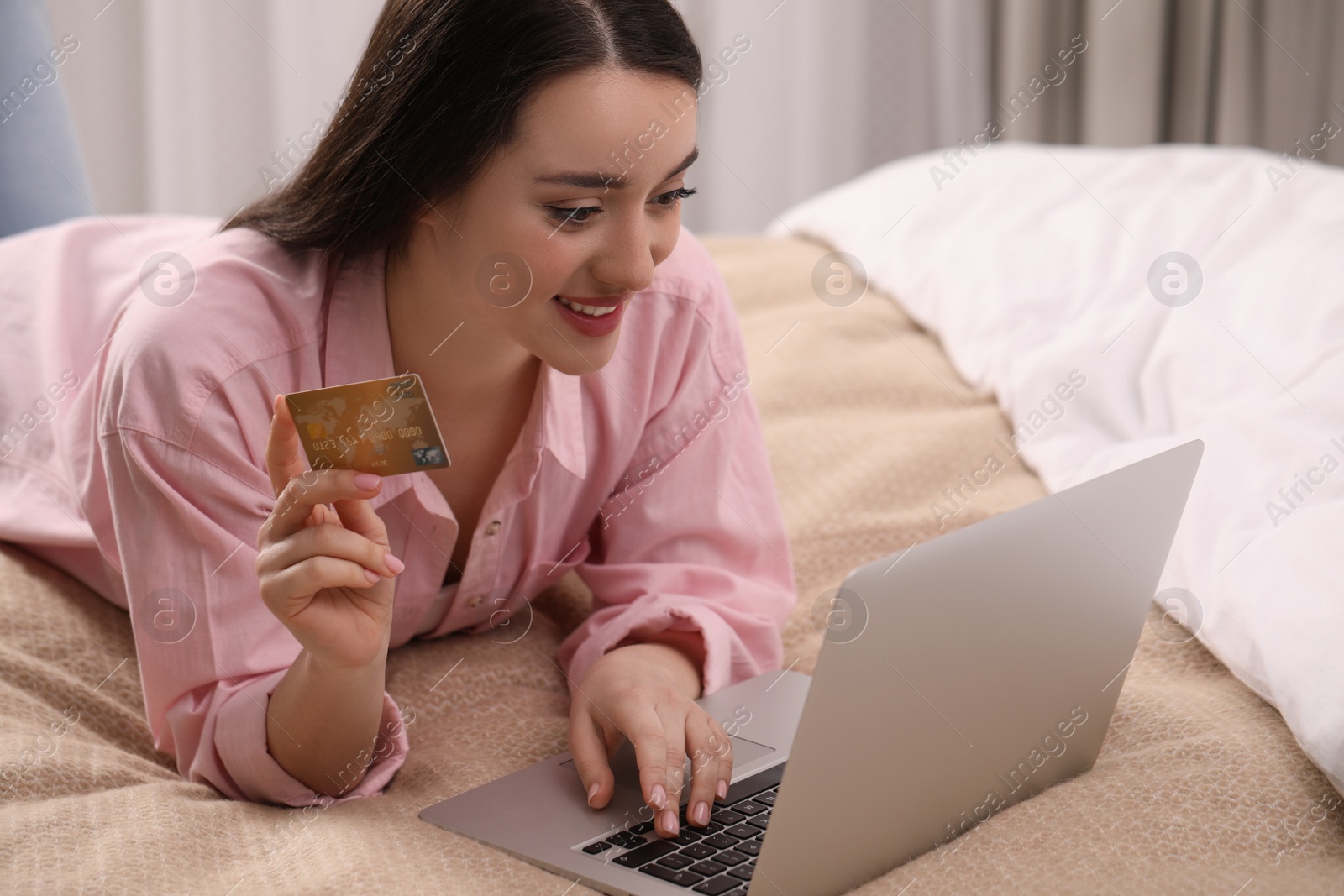 Photo of Woman with credit card using laptop for online shopping in bedroom