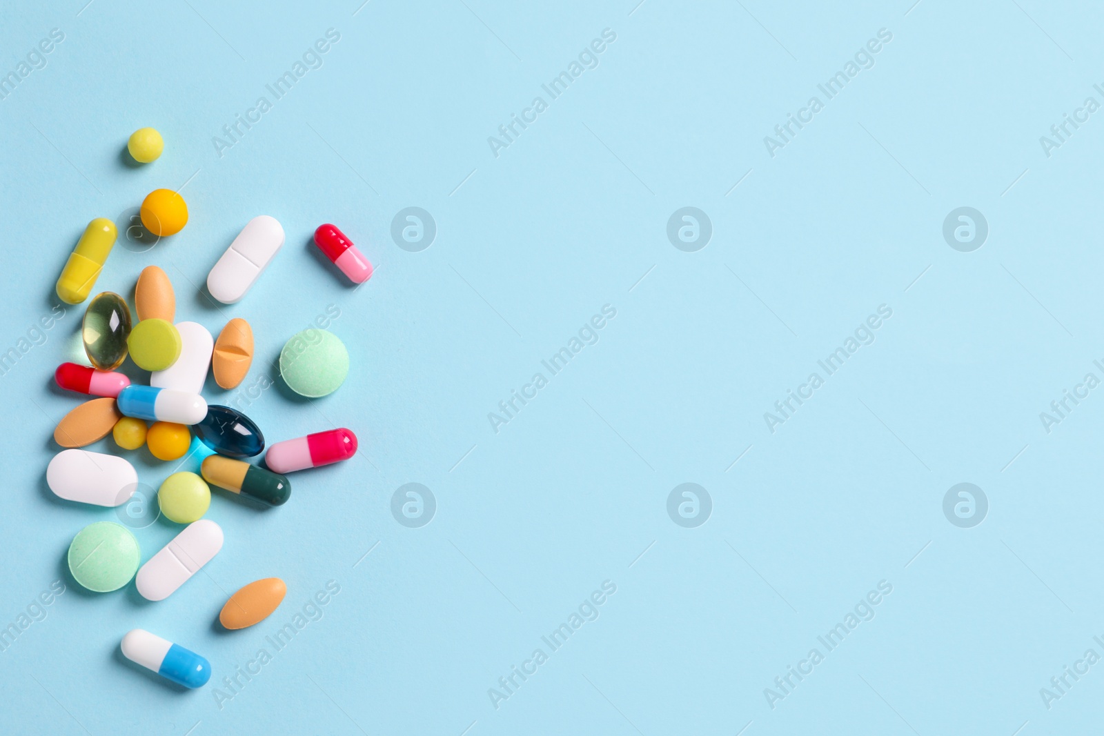 Photo of Many different pills on light blue background, flat lay. Space for text