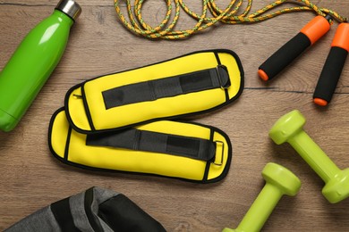 Photo of Yellow weighting agents and sport equipment on wooden table, flat lay