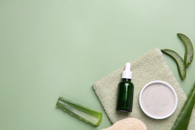 Cosmetic products, cut aloe leaves and towel on pale green background, flat lay. Space for text