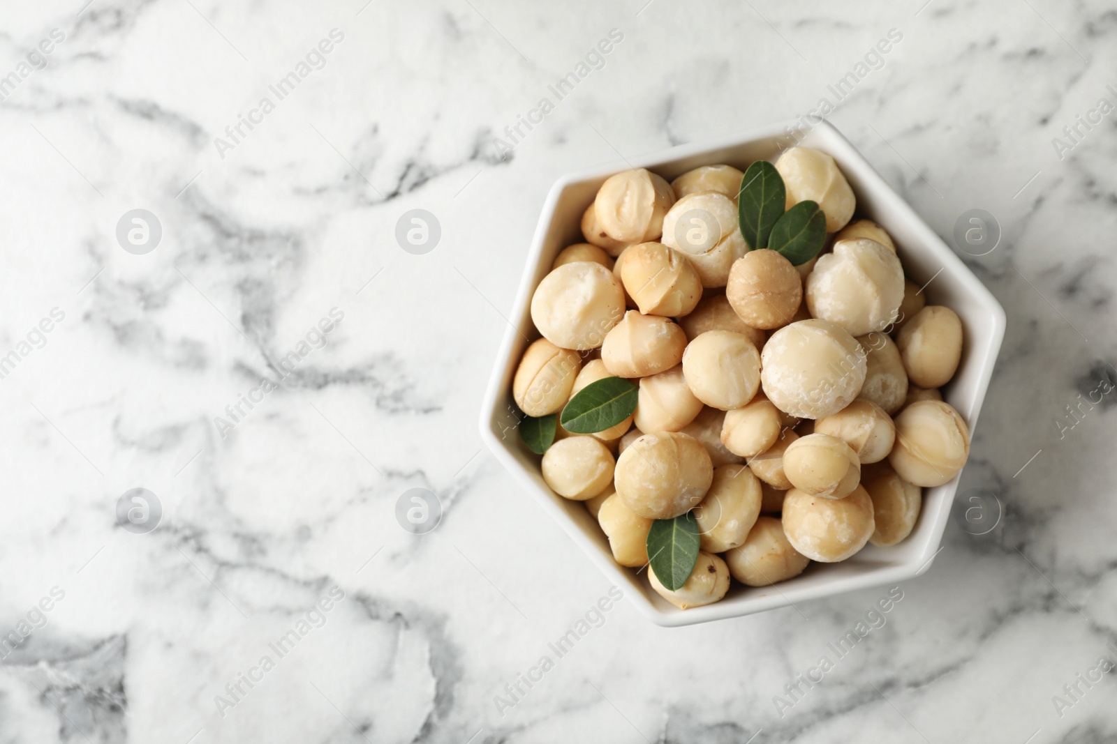 Photo of Bowl with shelled organic Macadamia nuts and space for text on marble background, top view