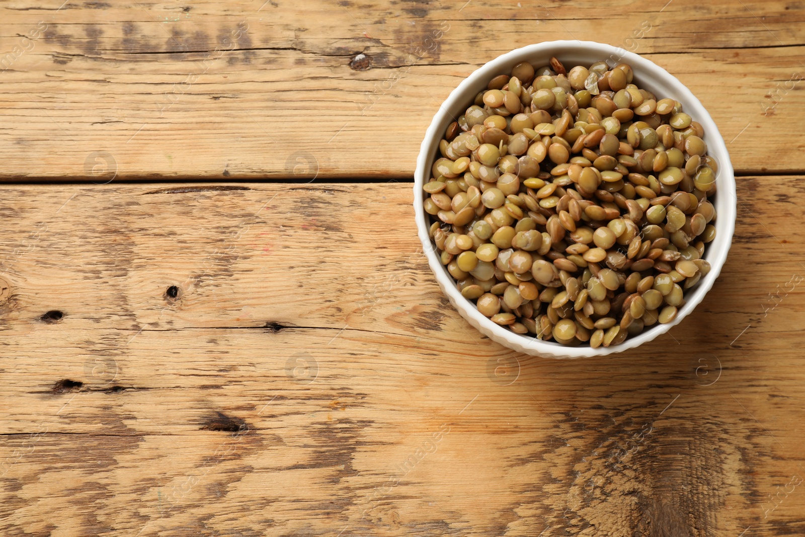 Photo of Delicious lentils in bowl on wooden table, top view. Space for text