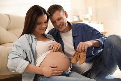 Photo of Young pregnant woman and her husband with baby's shoes at home