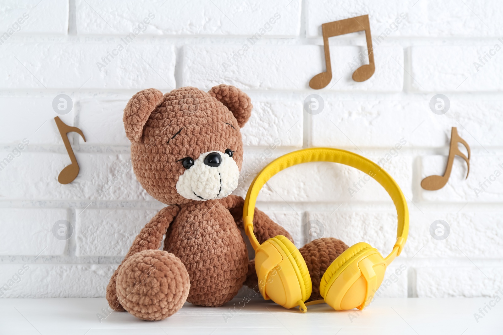 Photo of Baby songs. Toy bear and yellow headphones on white wooden table and notes