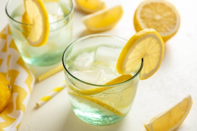 Soda water with lemon slices and ice cubes on white table