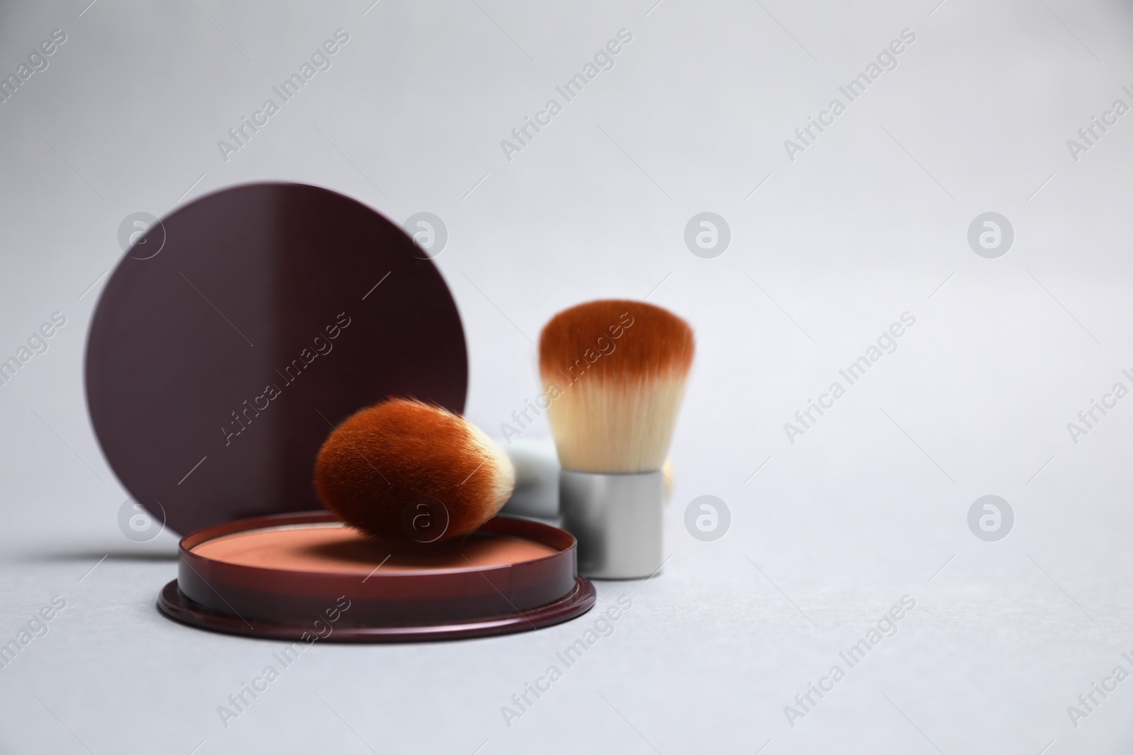 Photo of Open face powder and brushes on light grey background. Space for text