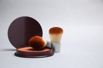 Photo of Open face powder and brushes on light grey background. Space for text