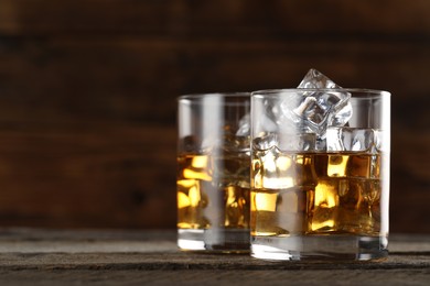 Whiskey with ice cubes in glasses on wooden table, closeup. Space for text