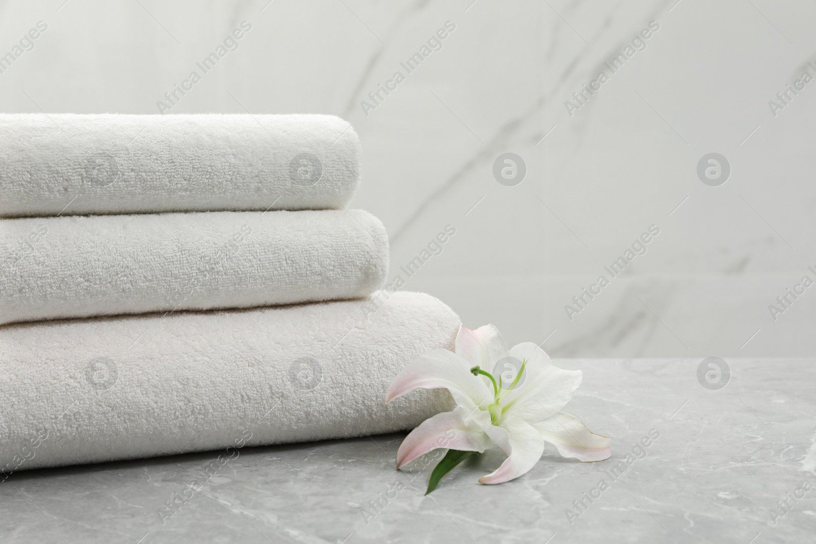 Photo of Stack of fresh towels with flower on grey table against light background. Space for text