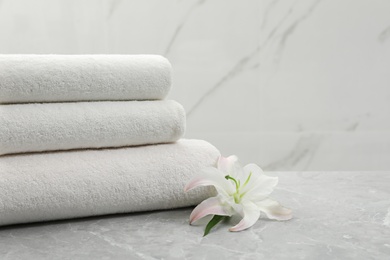 Stack of fresh towels with flower on grey table against light background. Space for text