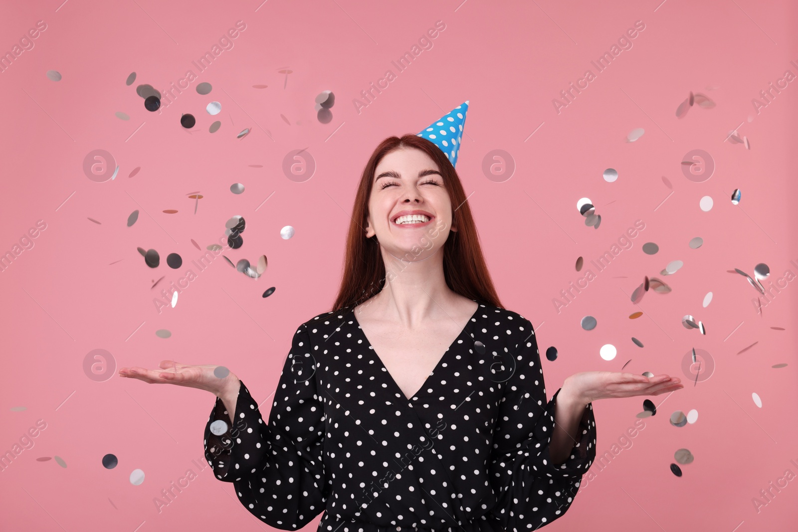 Photo of Happy woman in party hat and falling confetti on pink background