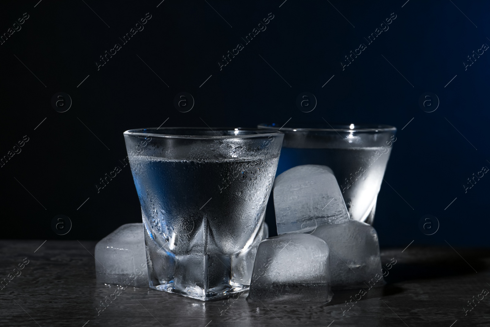 Photo of Vodka in shot glasses with ice on black table against dark background, closeup