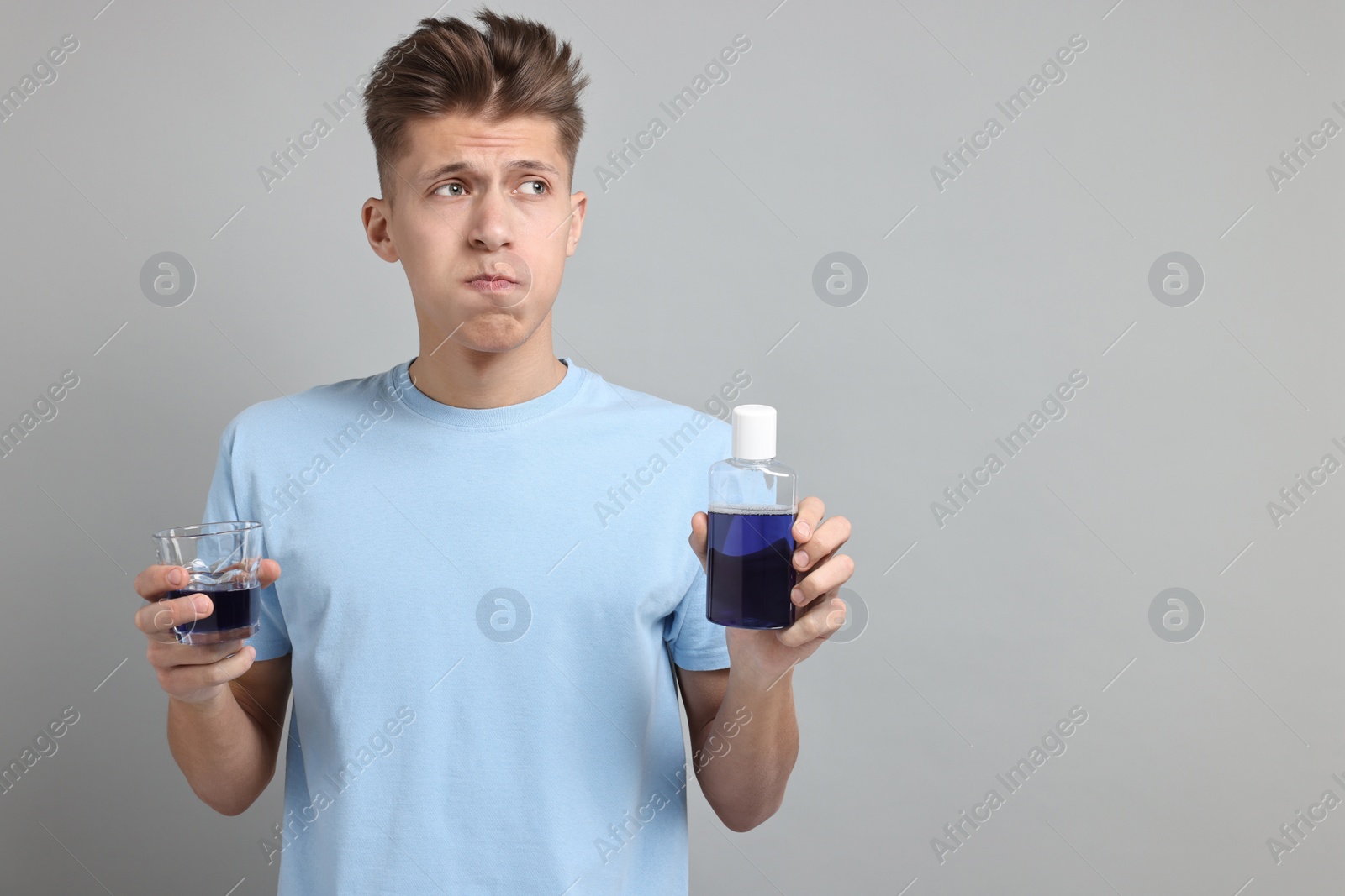 Photo of Young man using mouthwash on light grey background, space for text