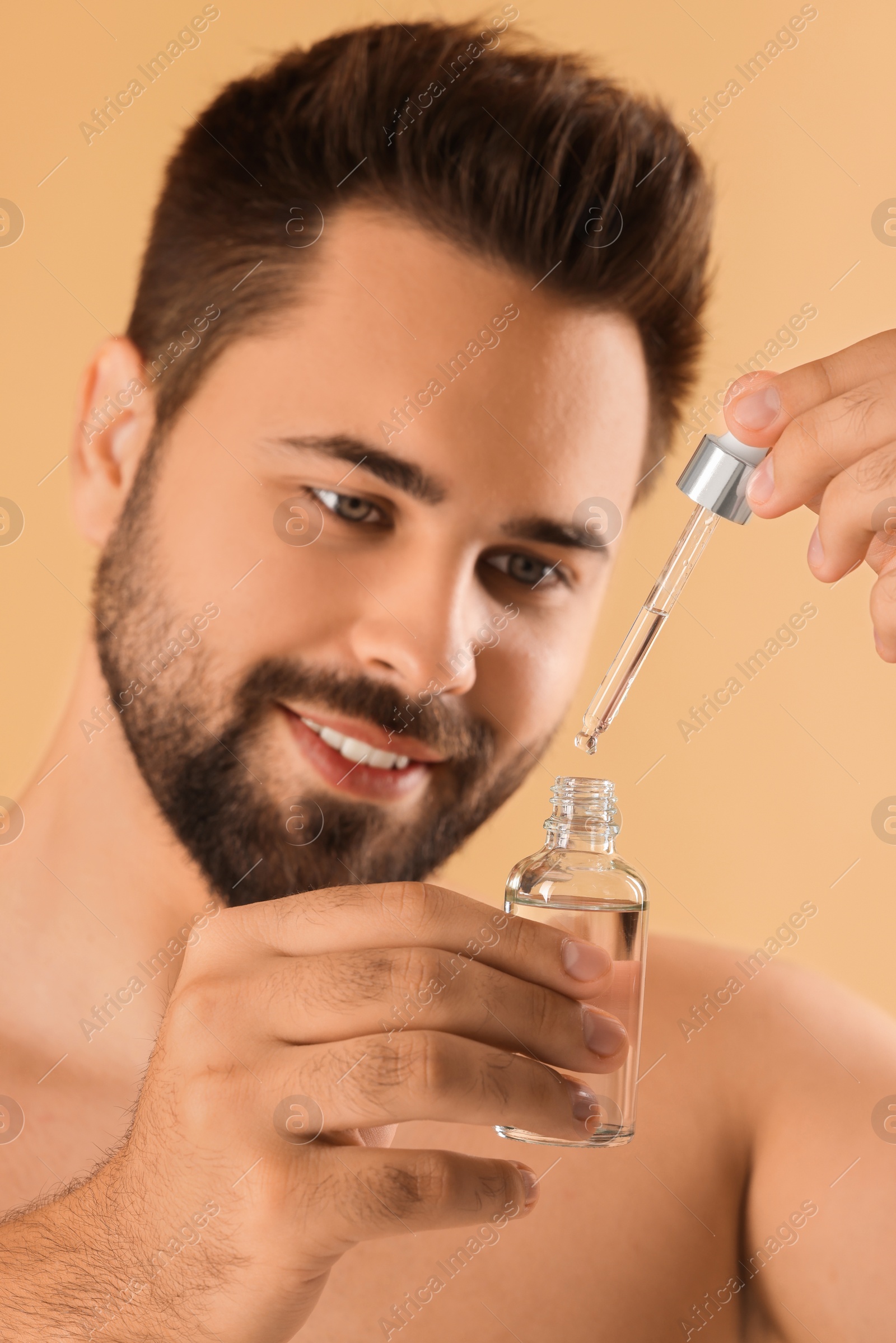 Photo of Handsome man with cosmetic serum in hands on beige background, selective focus