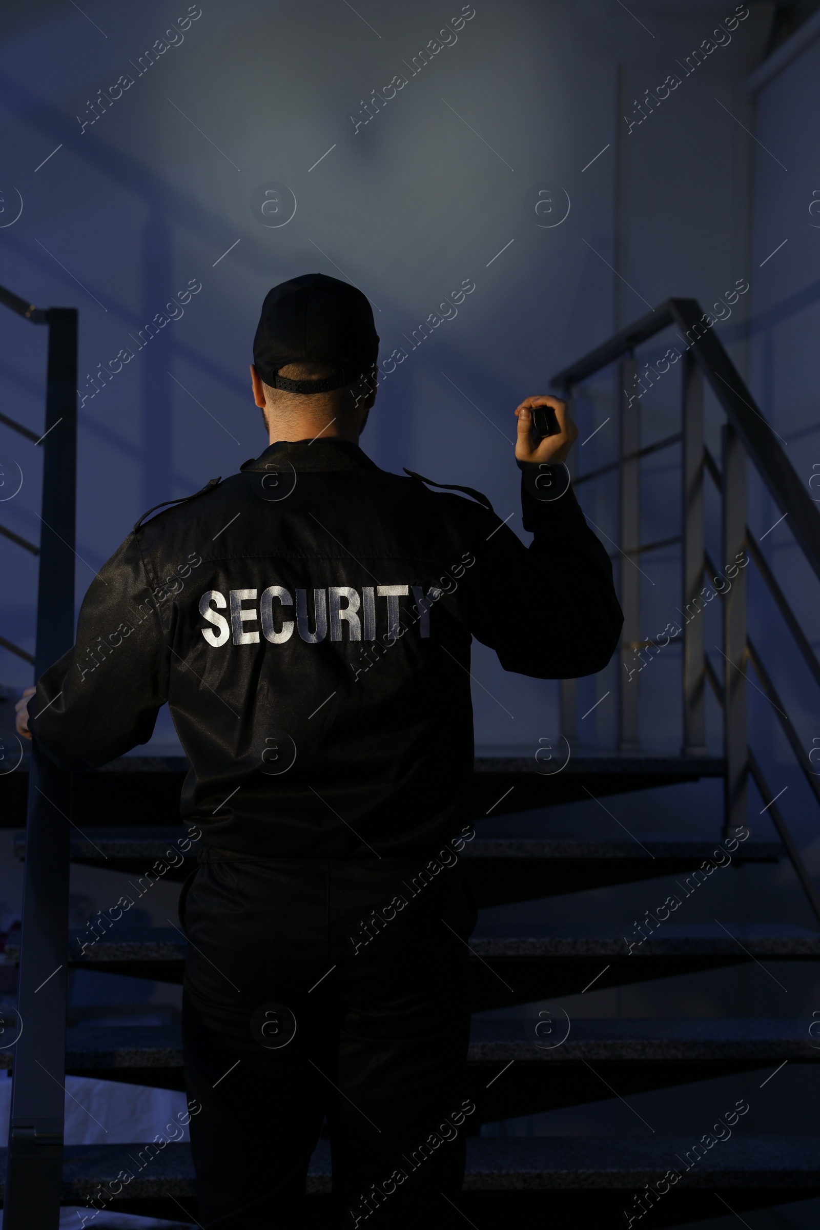 Photo of Male security guard with flashlight going up stairs in darkness