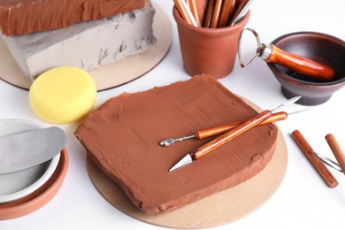 Photo of Clay and set of crafting tools on white textured table, closeup