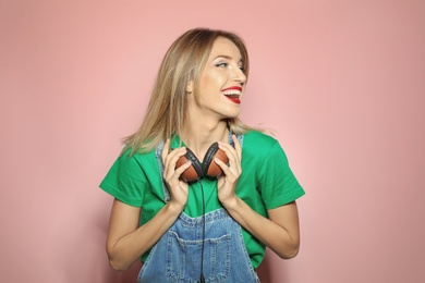 Beautiful young woman with healthy long blonde hair and headphones on color background