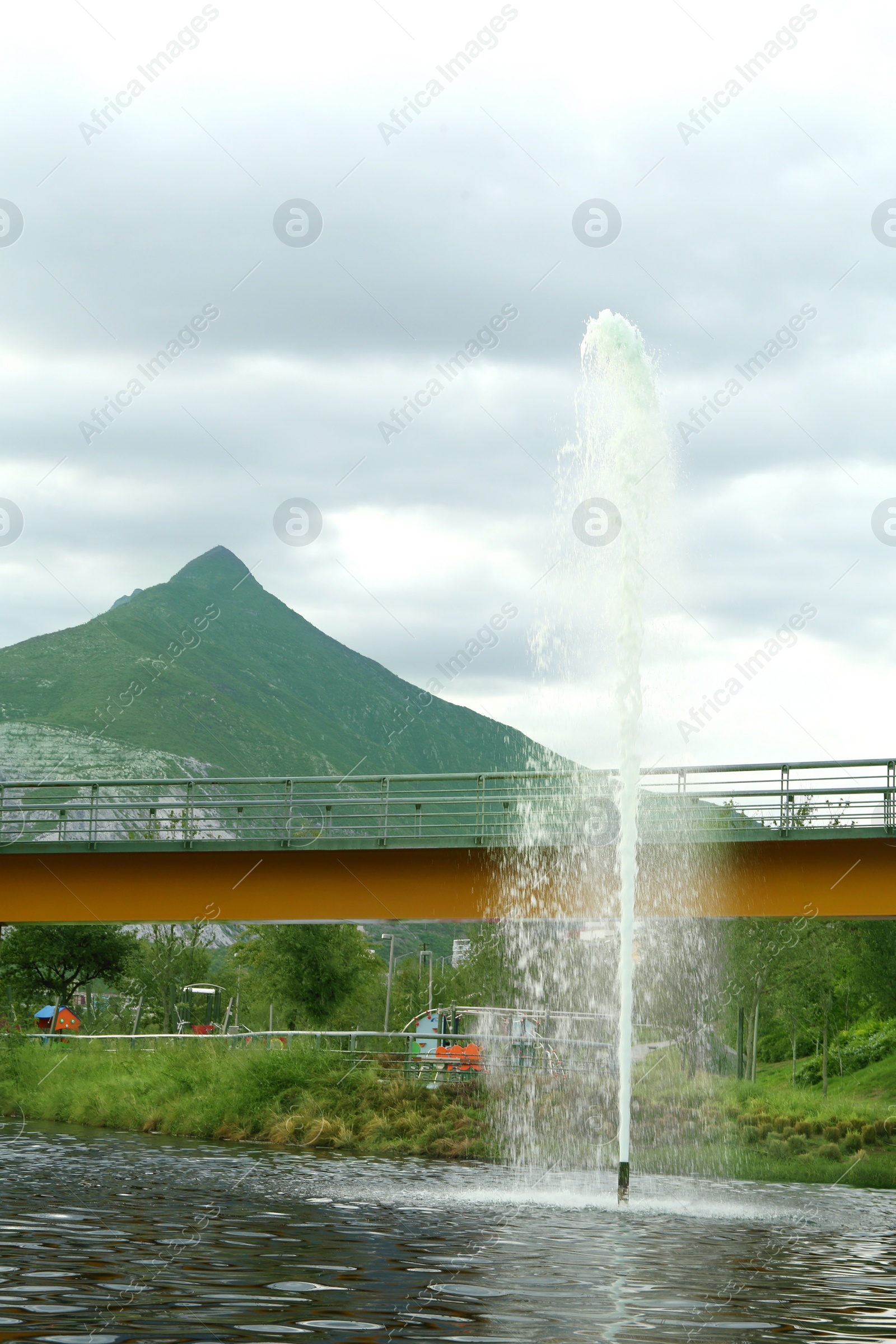 Photo of Beautiful view of bridge over pond with fountain in park near mountain