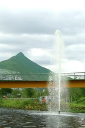 Beautiful view of bridge over pond with fountain in park near mountain