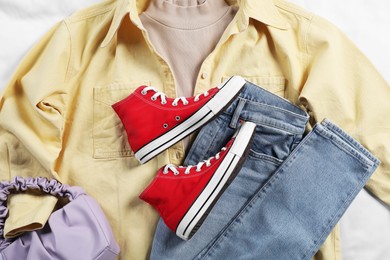 Pair of stylish red sneakers, clothes and bag on white fabric, flat lay