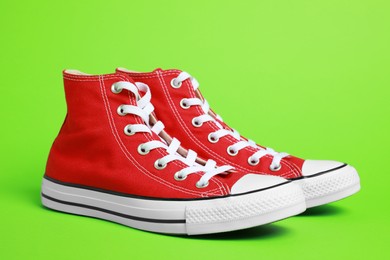 Photo of Pair of new stylish red sneakers on light green background