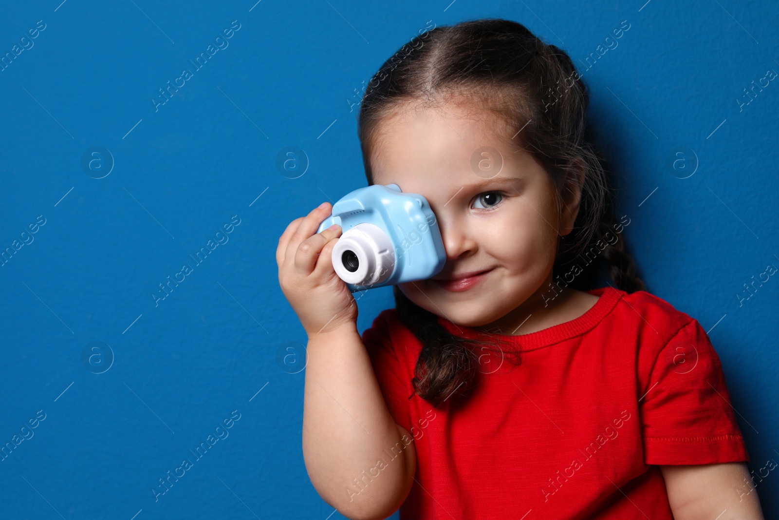 Photo of Little photographer taking picture with toy camera on blue background