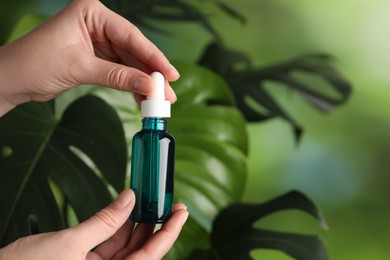 Photo of Woman with bottle of cosmetic serum on green background, closeup. Space for text