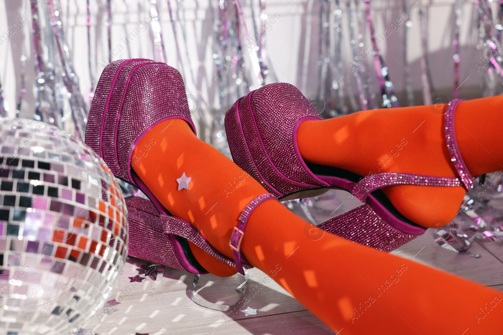 Photo of Woman in orange tights and pink high heeled shoes near disco ball indoors, closeup