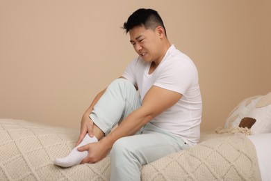 Photo of Asian man suffering from foot pain on bed indoors